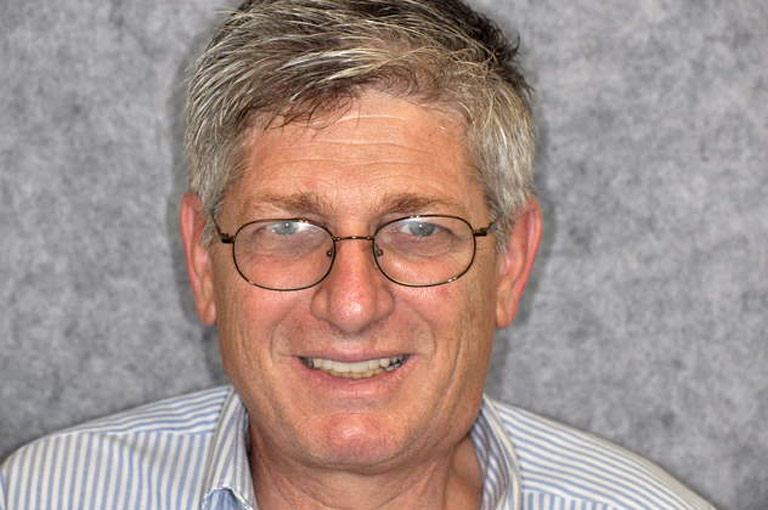 Headshot photo of gray-haired man with glasses smiling showing teeth after smile makeover