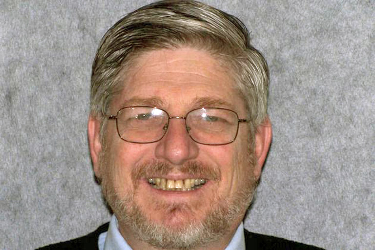 Headshot photo of gray-haired man with glasses smiling showing teeth before smile makeover
